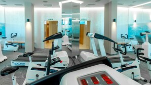 Et fitnesscenter med flere motionscykler og løbebånd, spejlvægge og et tydeligt skilt til udgang.