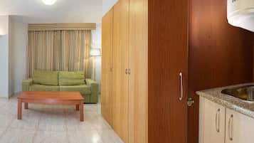 Habitación de hotel con una cama, un sofá, una mesita, una kitchenette con un lavamanos y un calentador de agua.