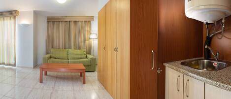 Una camera d'albergo con un letto, un divano, un tavolino, un angolo cottura con lavello e scaldabagno.