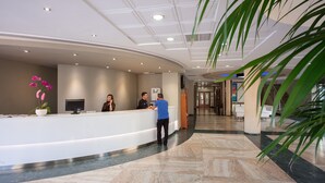 Et hotellets reception med en buet skranke, en potteorkidé og et moderne loftdesign.