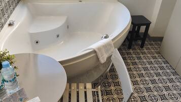 Une salle de bain avec une baignoire sur pieds, un petit tabouret et une plante décorée de bouteilles d’eau.