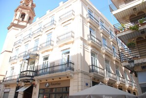 Um edifício de vários andares com varandas, uma torre do relógio e uma loja com um letreiro.