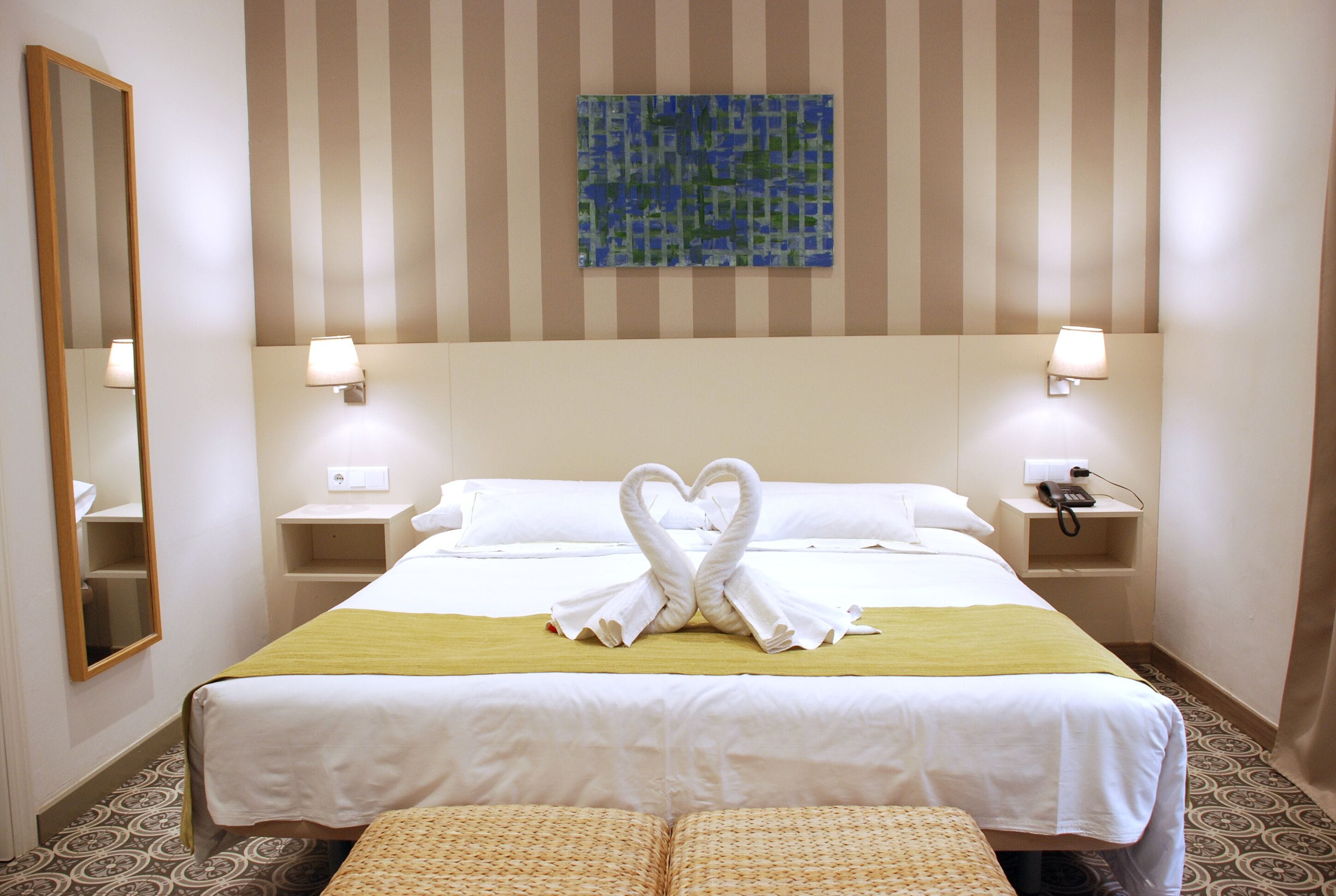 Habitación de hotel con una cama, dos mesitas de noche, un espejo, una obra de arte en la pared y un suelo estampado.