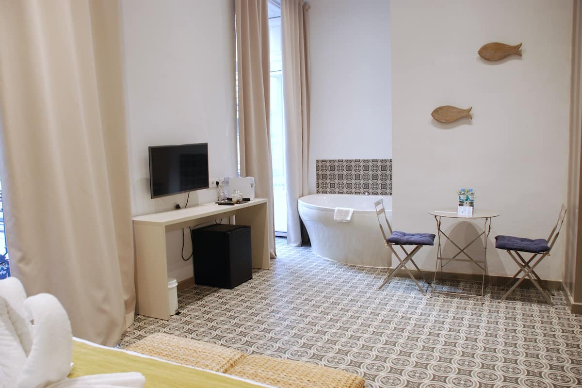 A hotel room with a bed, a desk with a TV, a bathtub, and two chairs.