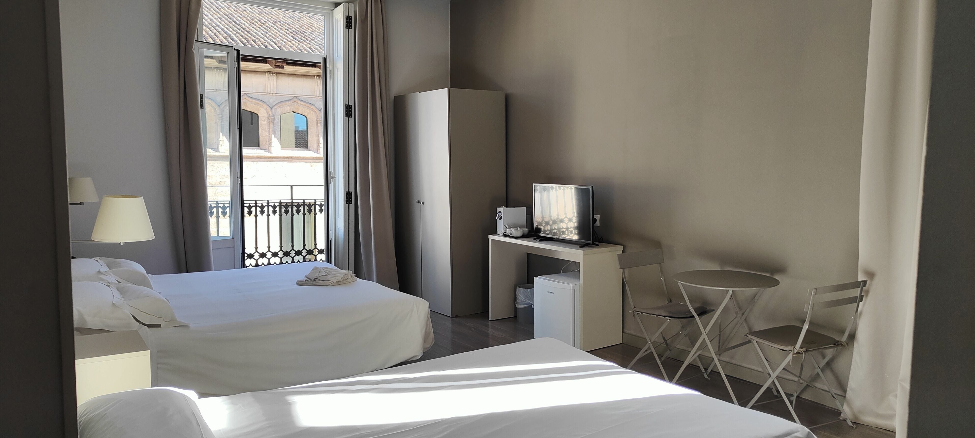 Una camera d'albergo con due letti, una scrivania con televisore, un tavolino e un balcone con ringhiera.