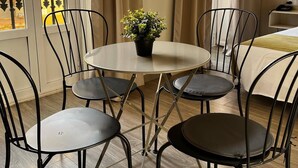 Um quarto com uma mesa redonda e quatro cadeiras, uma planta em vaso e uma cama com cabeceira branca.