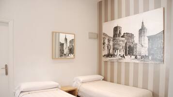 Habitación de hotel con dos camas individuales, un cuadro grande de un paisaje urbano enmarcado y una pared a rayas.