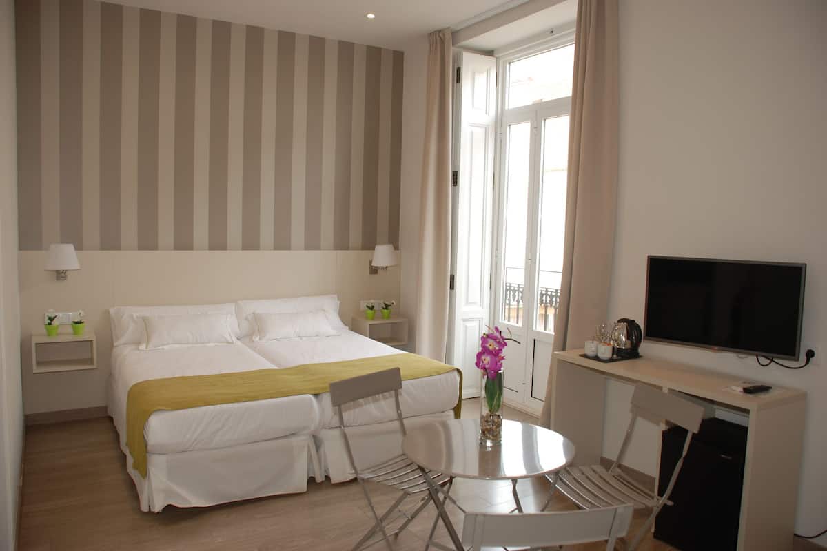 A hotel room with a double bed, a desk with a TV, a small table, and chairs.
