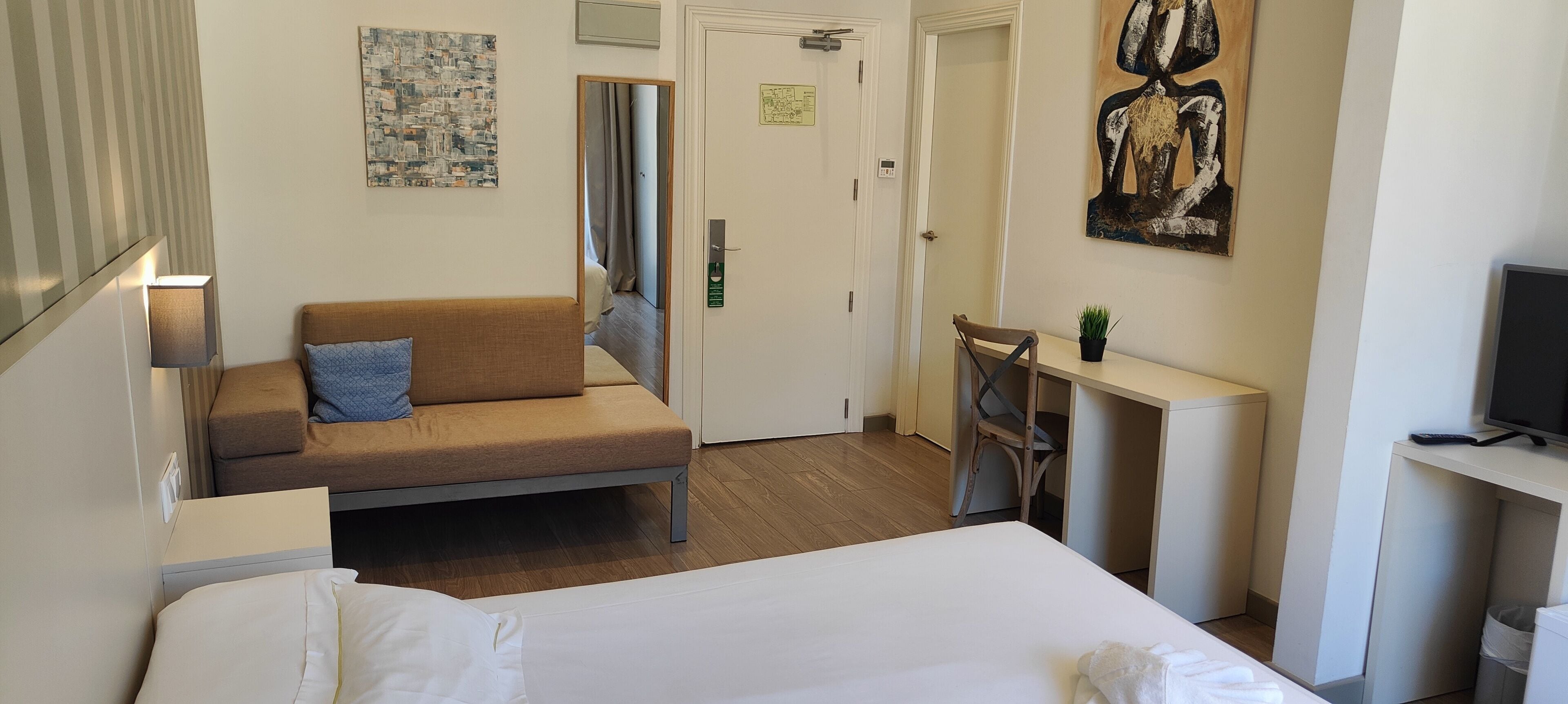 Une chambre d’hôtel équipée d’un lit, d’un canapé, d’un bureau, d’une télévision et décorée avec des œuvres d’art aux murs.