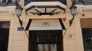 A entrada do Hotel Boutique San Lorenzo, com uma placa acima da porta, duas luminárias fixadas na parede e uma placa indicando a localização como Plaza de Sant Llorenc.