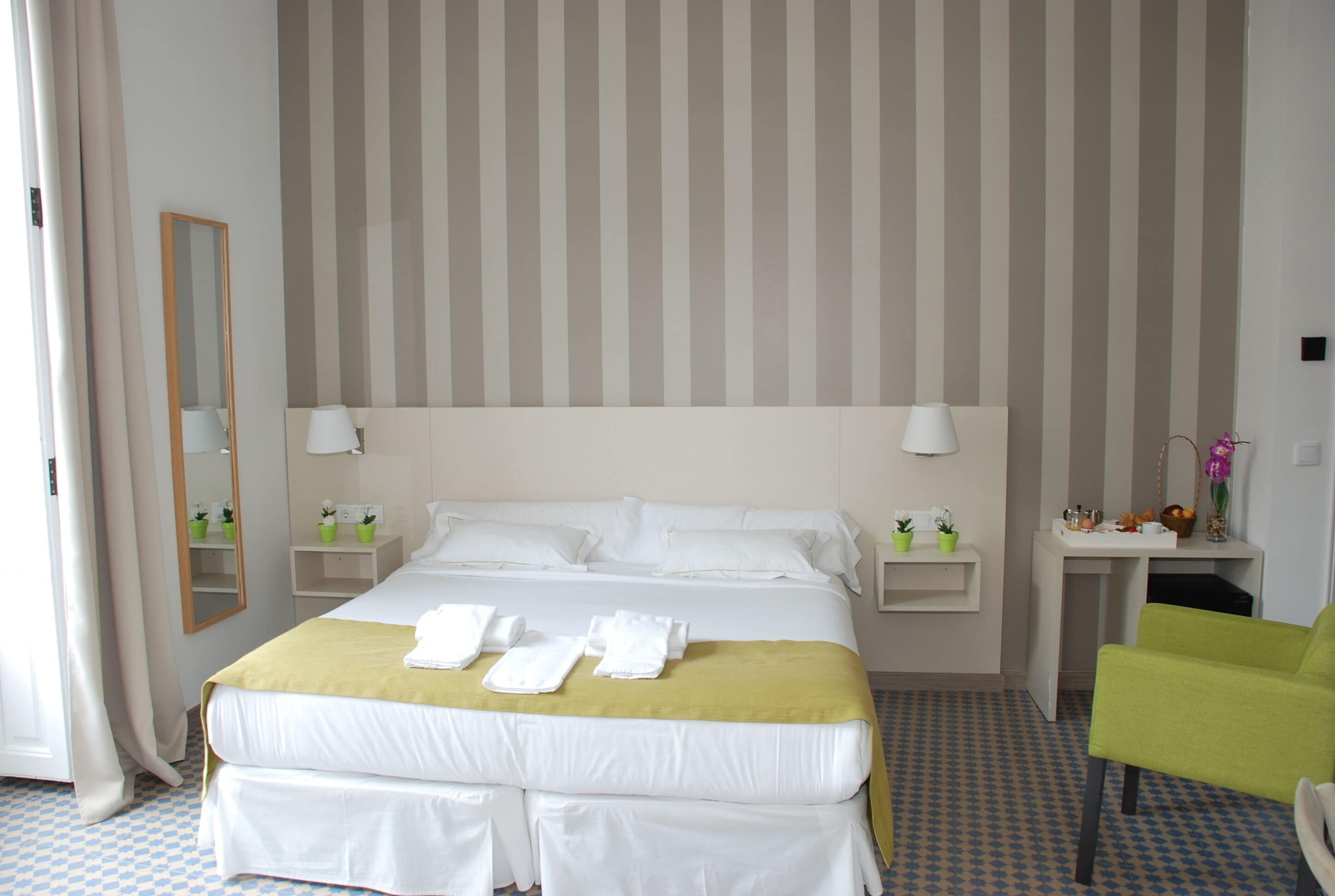 A hotel room with a large bed, two bedside tables, a mirror, and a green chair.