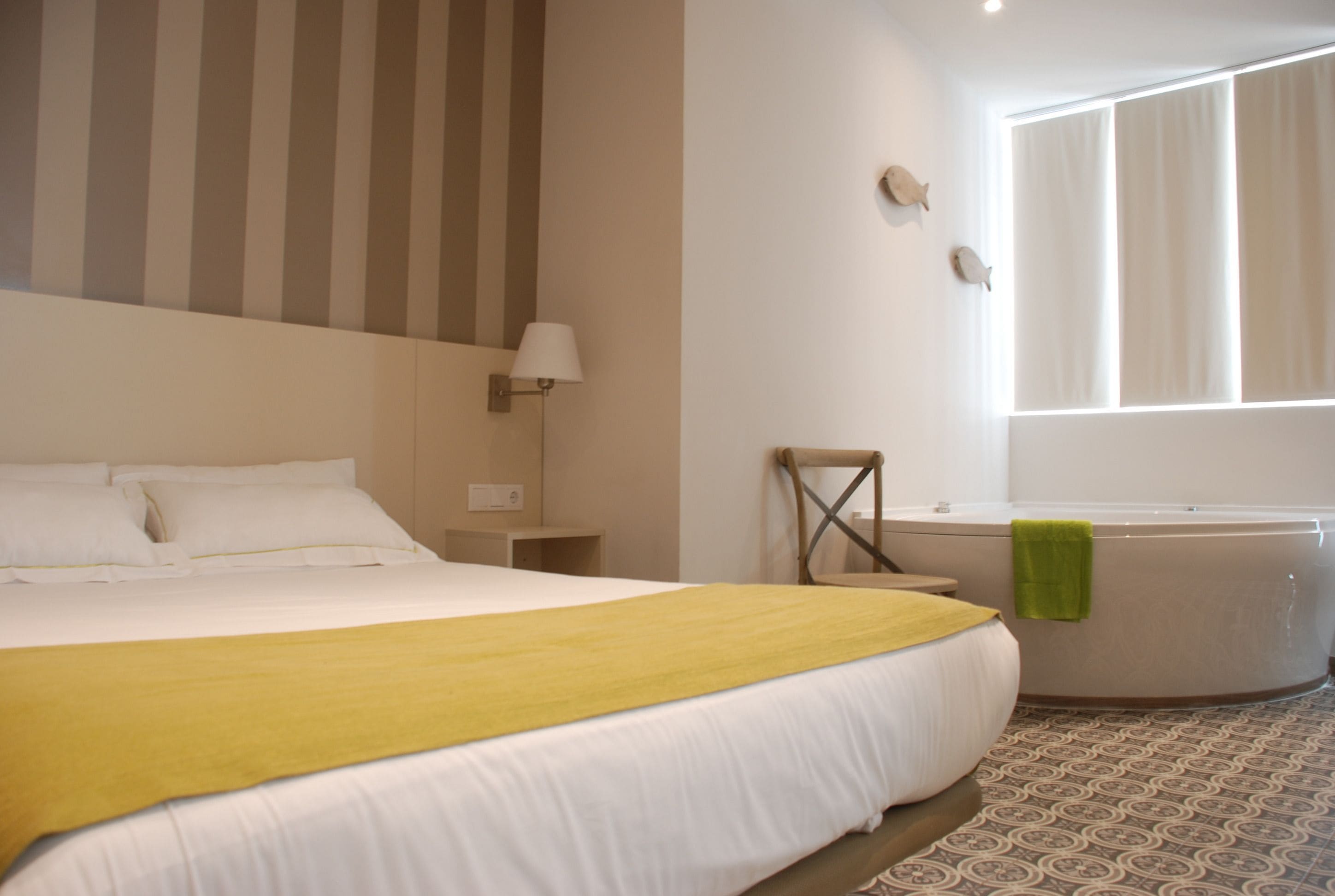 Een hotelkamer met een groot bed, een nachtkastje, een lamp, een stoel, een badkuip en een raam met gordijnen.