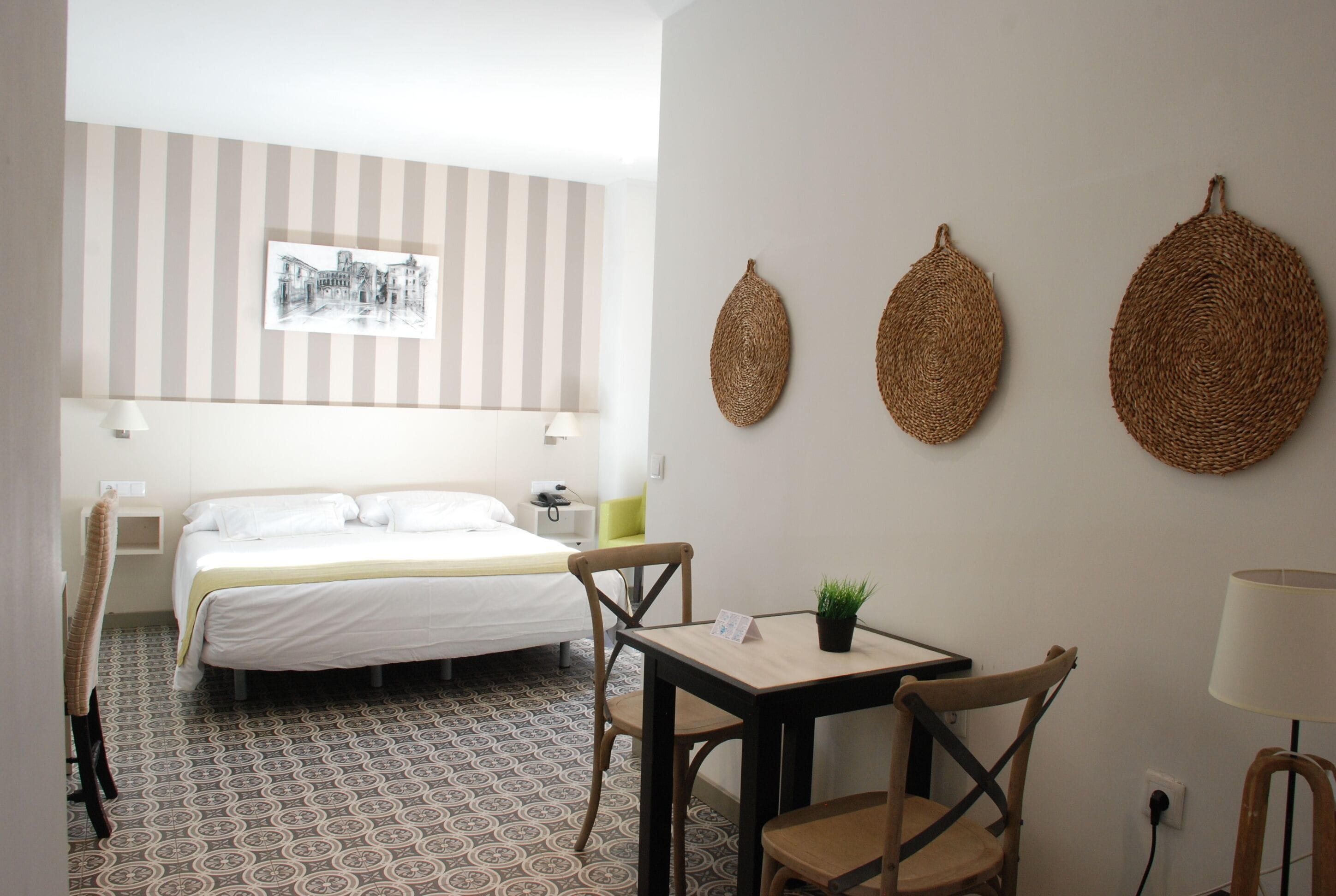 A hotel room with a bed, a table with a plant, and three woven wall decorations.