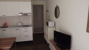 A compact kitchen with white cabinets, a toaster, a microwave, and a wooden dining table. - rent-a-home Schweizergasse (Basel)