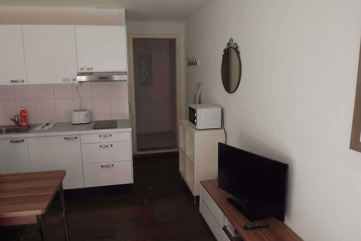 A compact kitchen with white cabinets, a toaster, a microwave, and a wooden dining table.