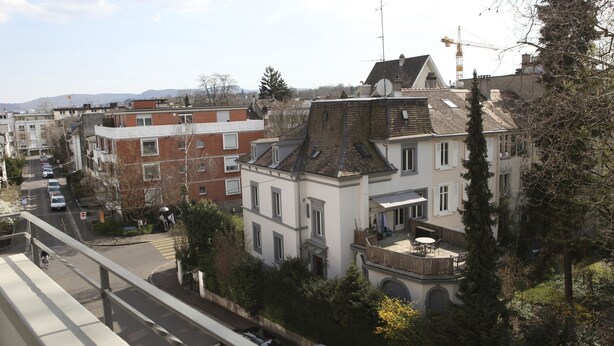A residential area with a mix of modern and traditional architecture, including a prominent white building with a balcony and a red brick building. - rent-a-home Schweizergasse (Basel)
