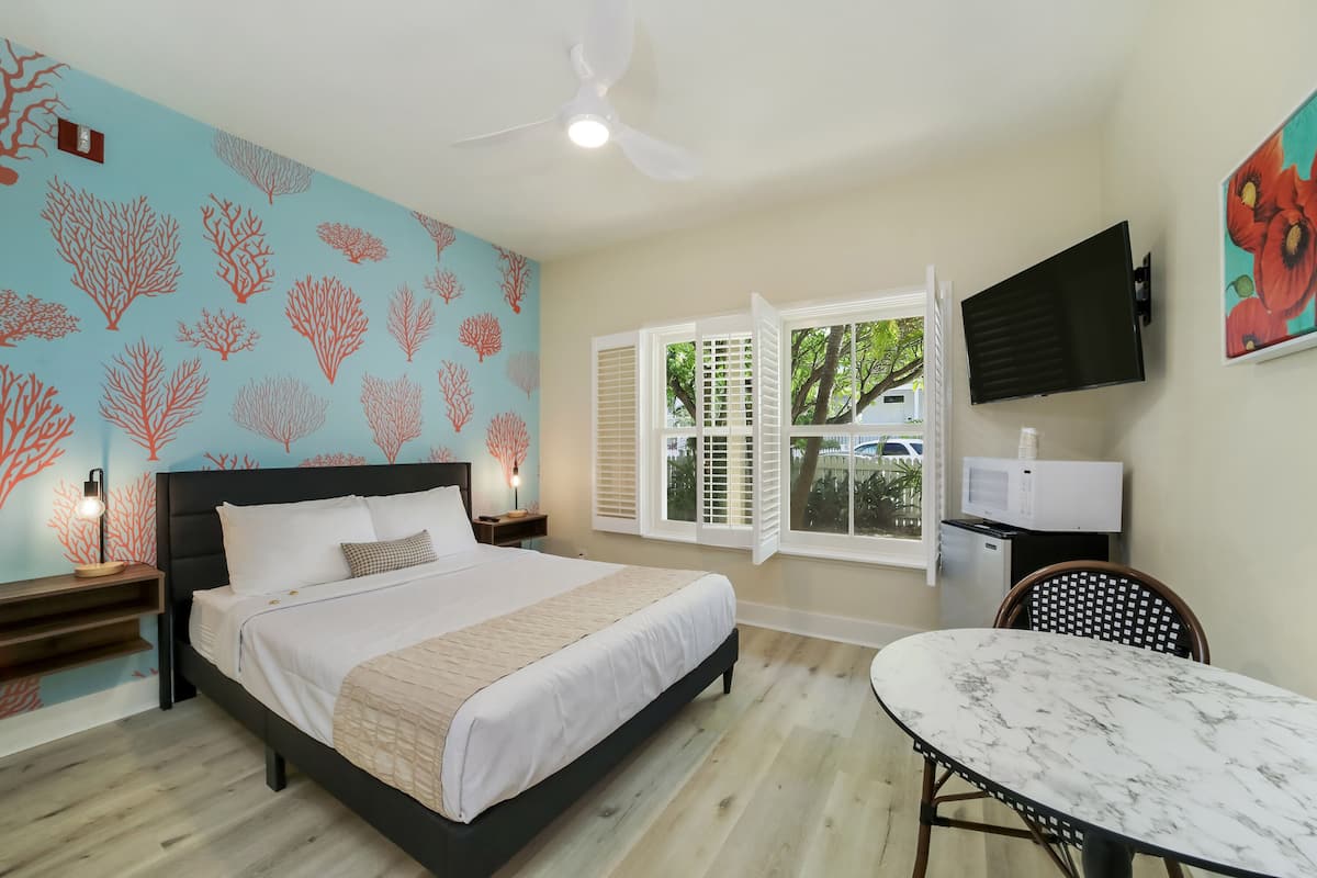 Un dormitorio con cama, ventilador de techo, televisor, mesa de comedor y ventana con contraventanas.