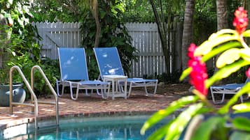 A pool area with lounge chairs and a white picket fence.