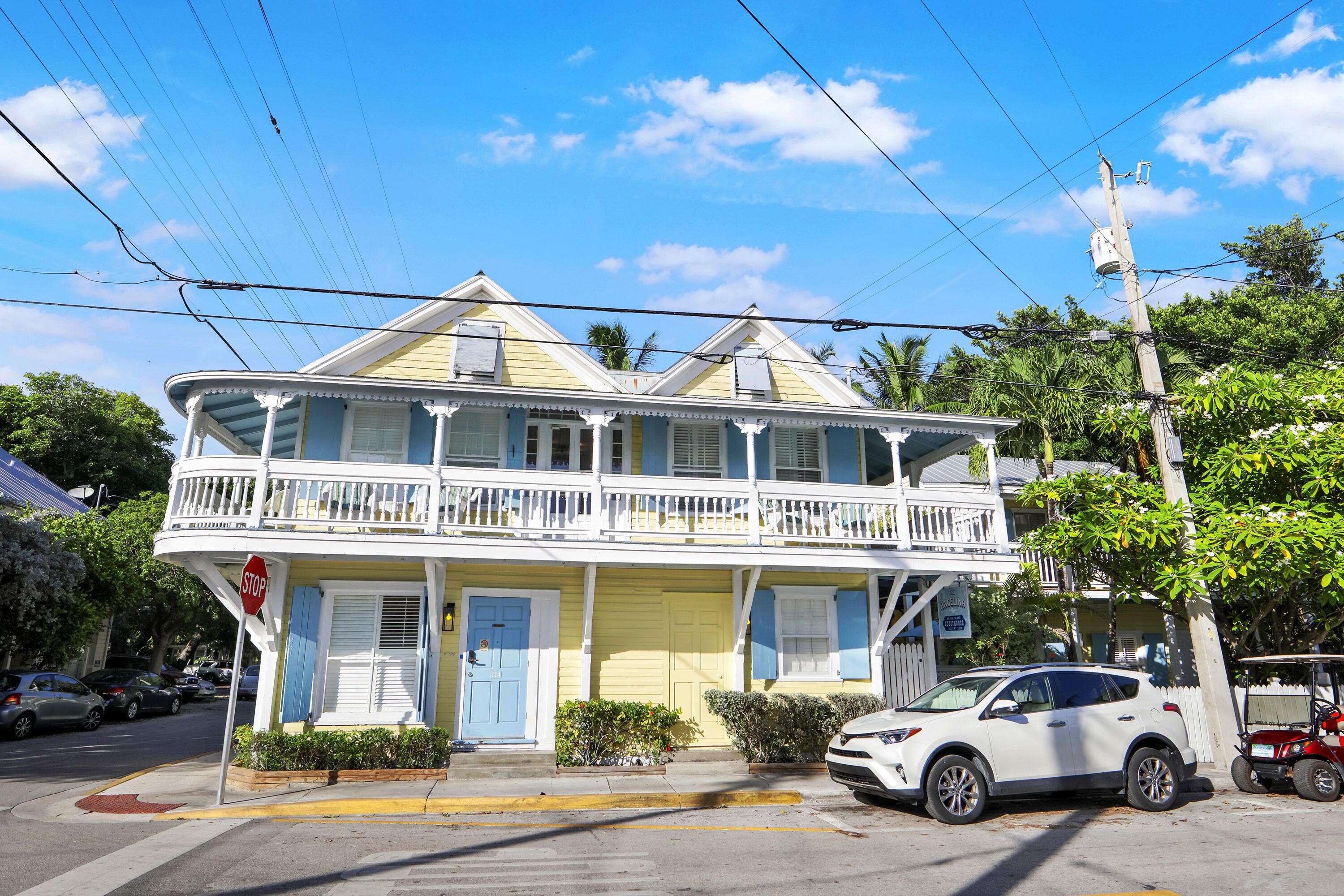 A two-story building with a balcony, a stop sign, and a white car parked in front.
