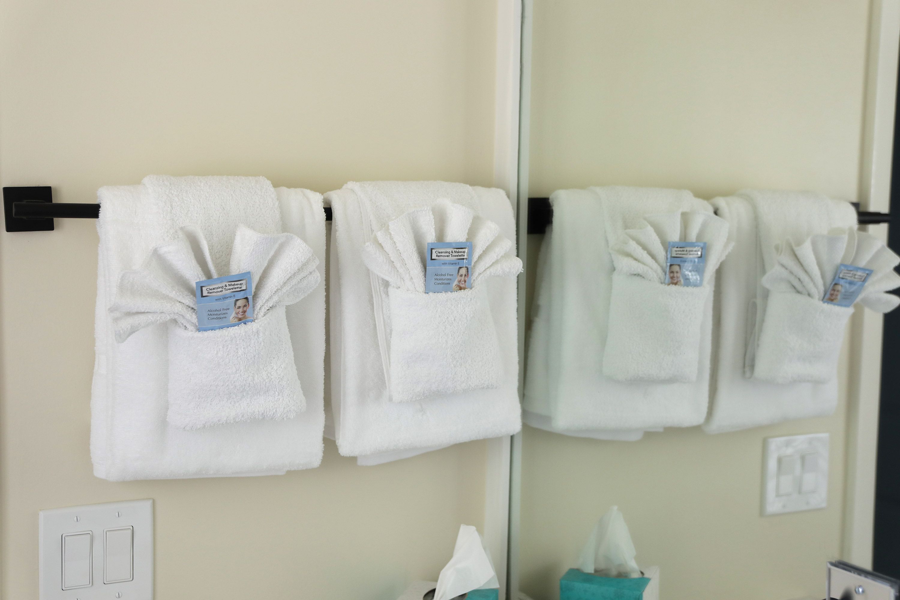 A bathroom with white towels hanging on a rack, a mirror, a tissue box, and a light switch.