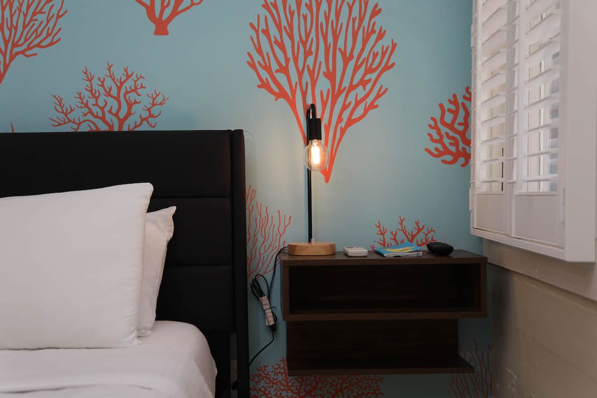 Una habitación con cama, mesita de noche y lámpara, y una pared decorada con motivos de coral.