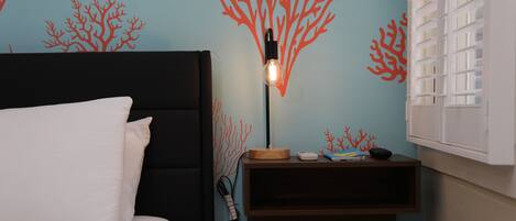 Una habitación con cama, mesita de noche y lámpara, y una pared decorada con motivos de coral.