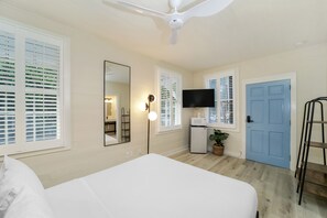 A bedroom with a bed, a ceiling fan, a TV, and a blue door.