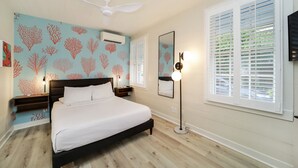 Un dormitorio con cama, ventilador de techo, equipo de aire acondicionado, mesita de noche, lámpara y ventana con persianas.