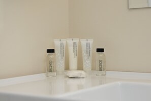 Een badkamer met een witte wastafel, drie flesjes bodylotion en een witte handdoek.