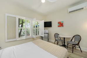 A hotel room with a bed, a small table with two chairs, a TV, and a window with shutters. - Tranquility Guest House  (Key West)