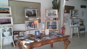 A gallery with framed artworks on display, a wooden table with books and a vase, and a fire extinguisher in the background. - Hotel Lux Modena (Modena)