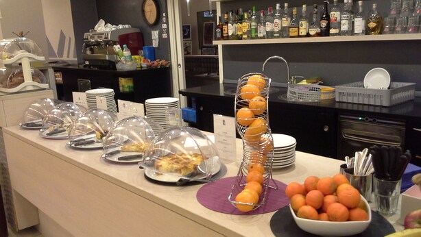 A buffet setup with covered food items, a fruit display, and a bar area with various bottles. - Hotel Lux Modena (Modena)