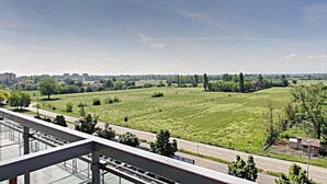 A view from a balcony overlooking a green field with a road and distant buildings. - Hotel Lux Modena (Modena)