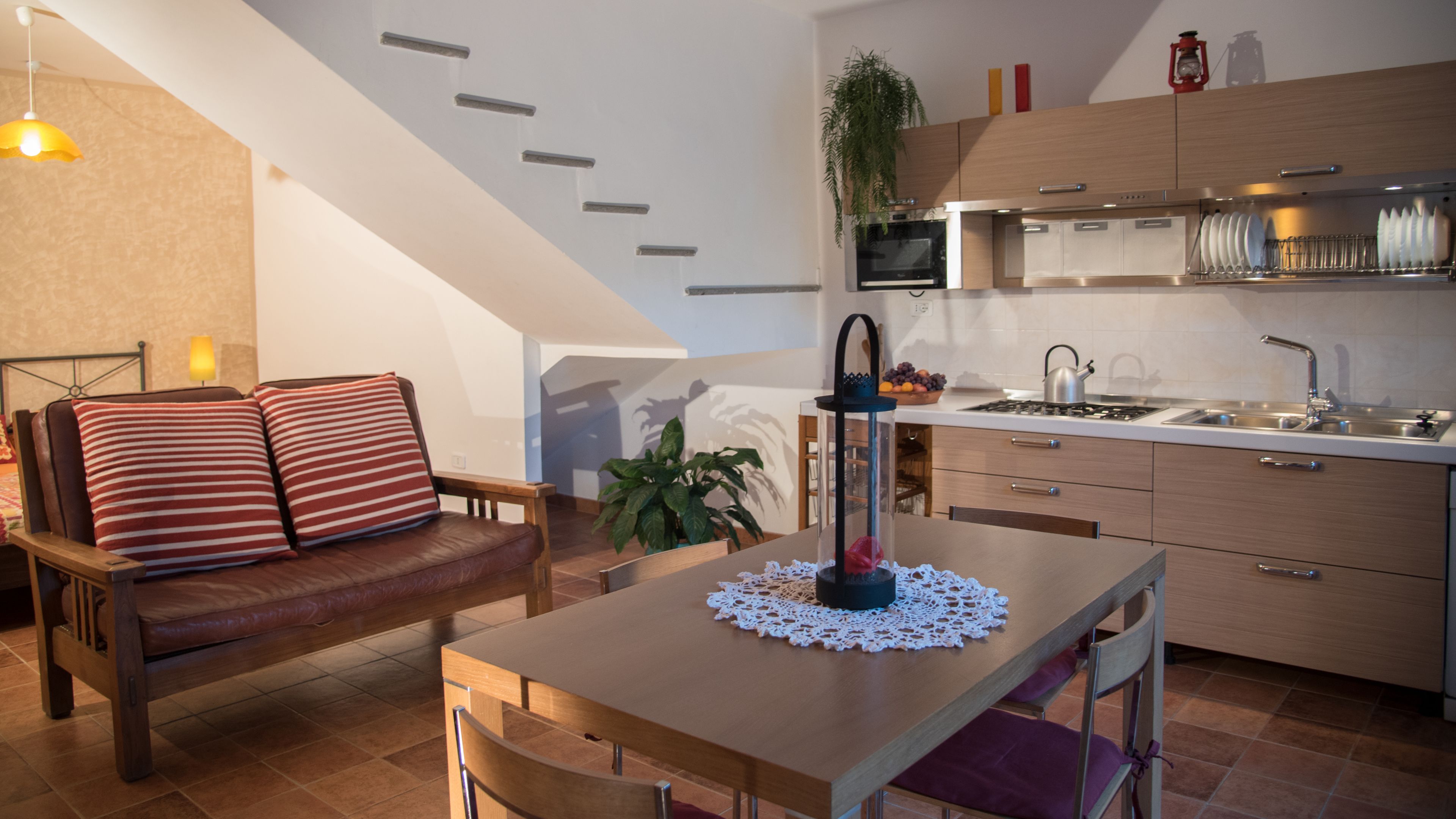 A modern kitchen with a dining area, including a wooden table, chairs, and a sofa with striped cushions.