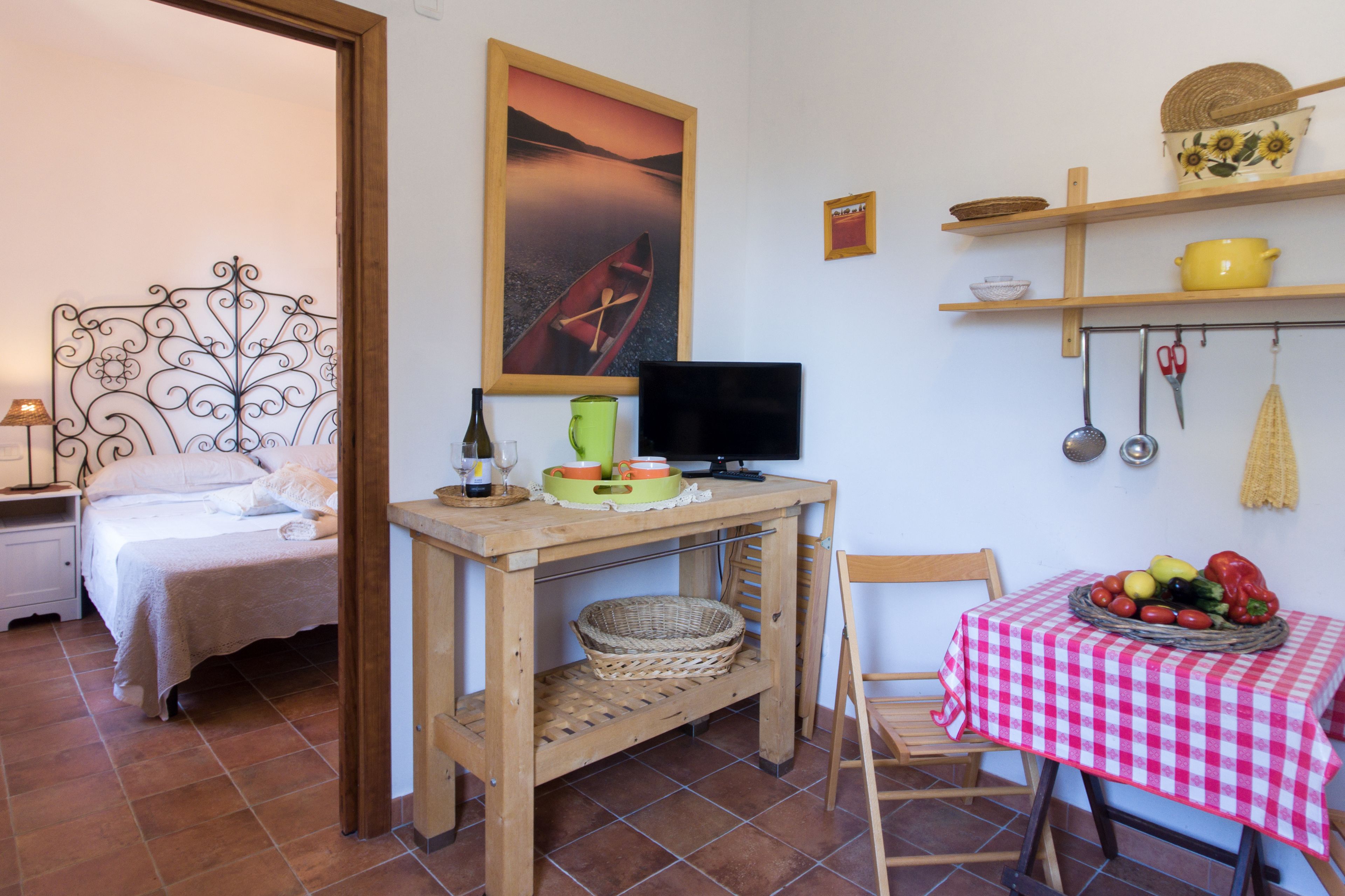 A bedroom with a bed, a bedside table with a lamp, a TV, and a breakfast table with a checkered tablecloth.