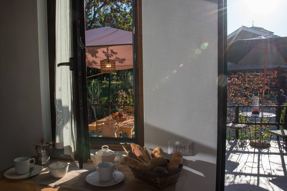 Ein Essbereich mit Tisch, gedeckten Tee-Tellern, einem Brotkorb und Blick auf eine Terrasse mit Sonnenschirmen.