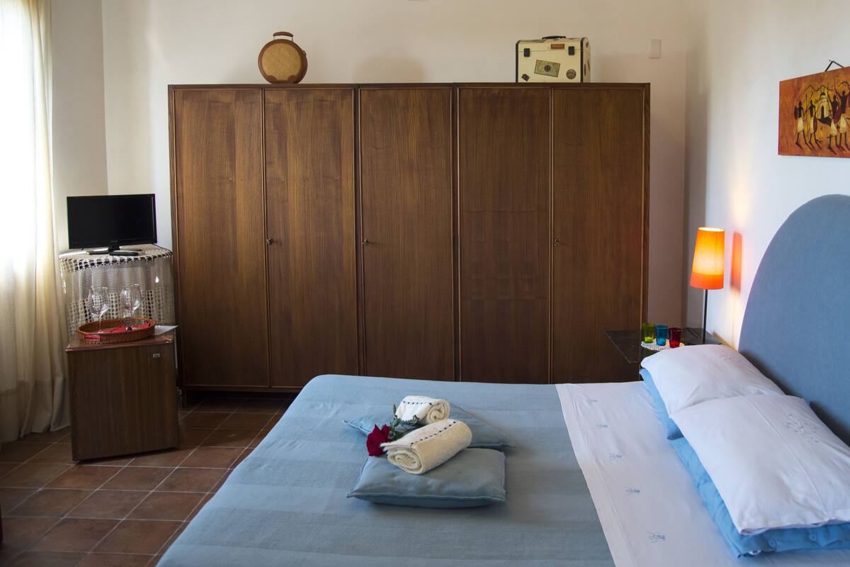 Ein Hotelzimmer mit Bett, Kleiderschrank, Schreibtisch mit Lampe und einem Gemälde an der Wand.