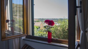 A window with a view of a landscape, a red vase with flowers, and a curtain. - Villa Tresino Appartamenti B&B (Castellabate)