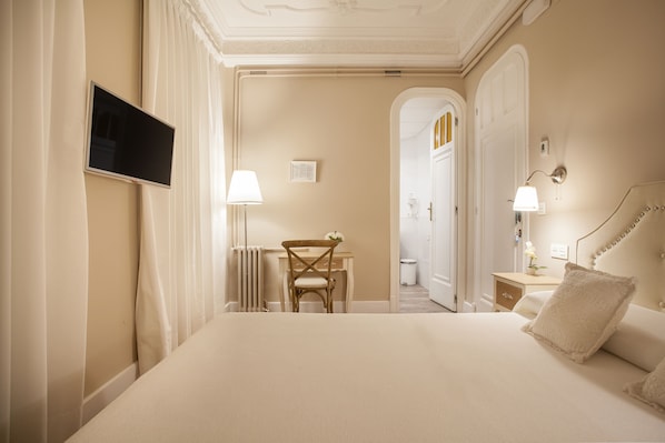 Habitación de hotel con una cama grande, un escritorio con una silla, un televisor montado en la pared y una lámpara en la mesita de noche.