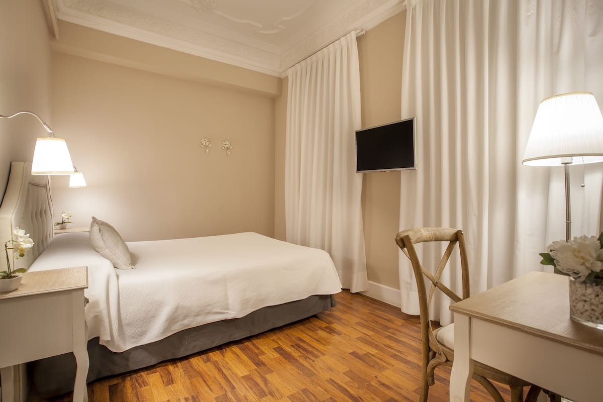 A hotel room with a bed, a desk, a chair, a TV, and a lamp.