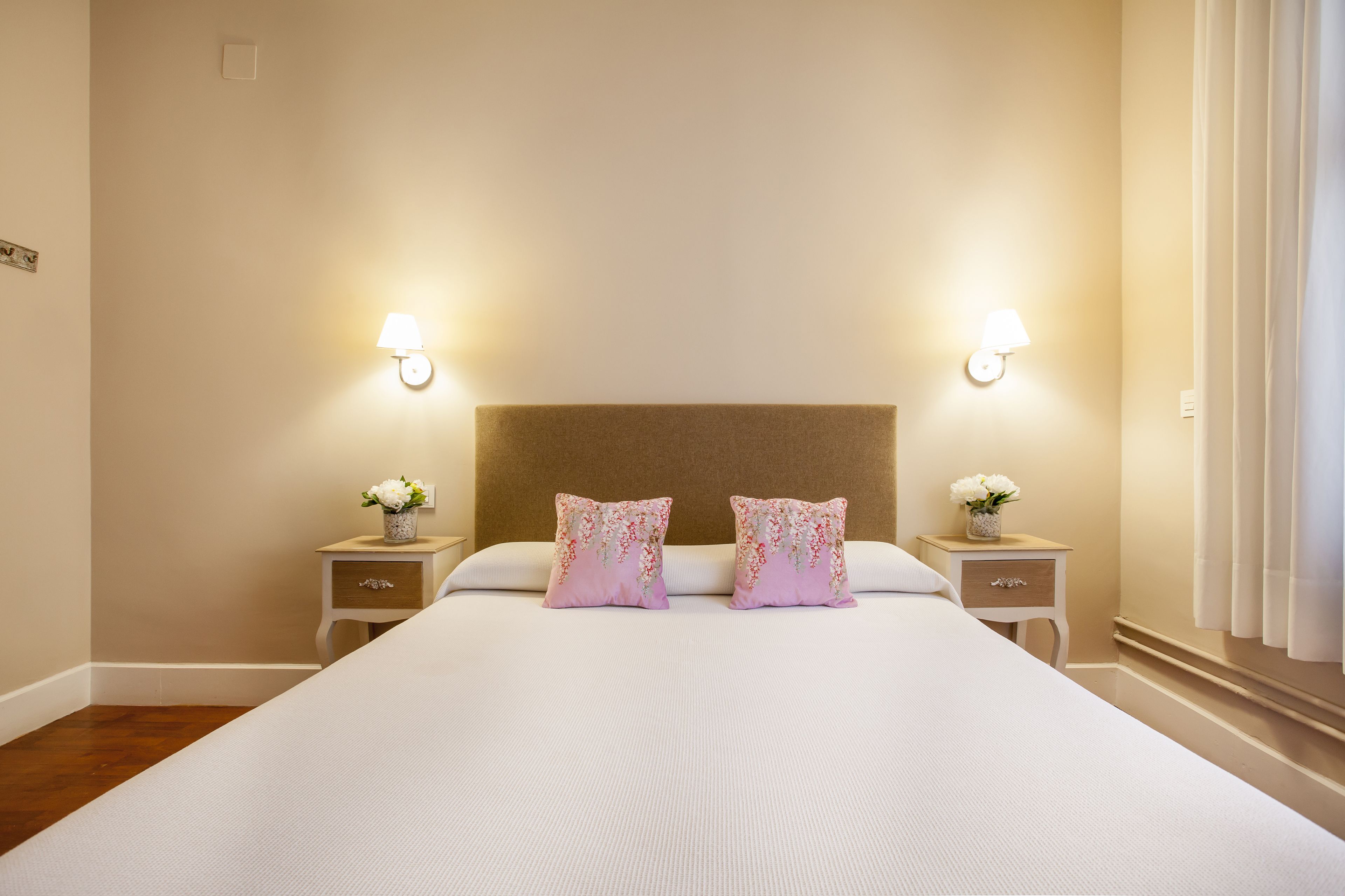 Hotellihuone, jossa on suuri sänky, kaksi yöpöytää valaisimineen ja sängynpääty.