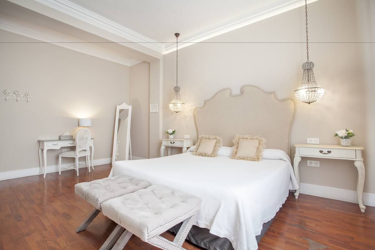 A bedroom with a large bed, two bedside tables, a chair, and a desk.