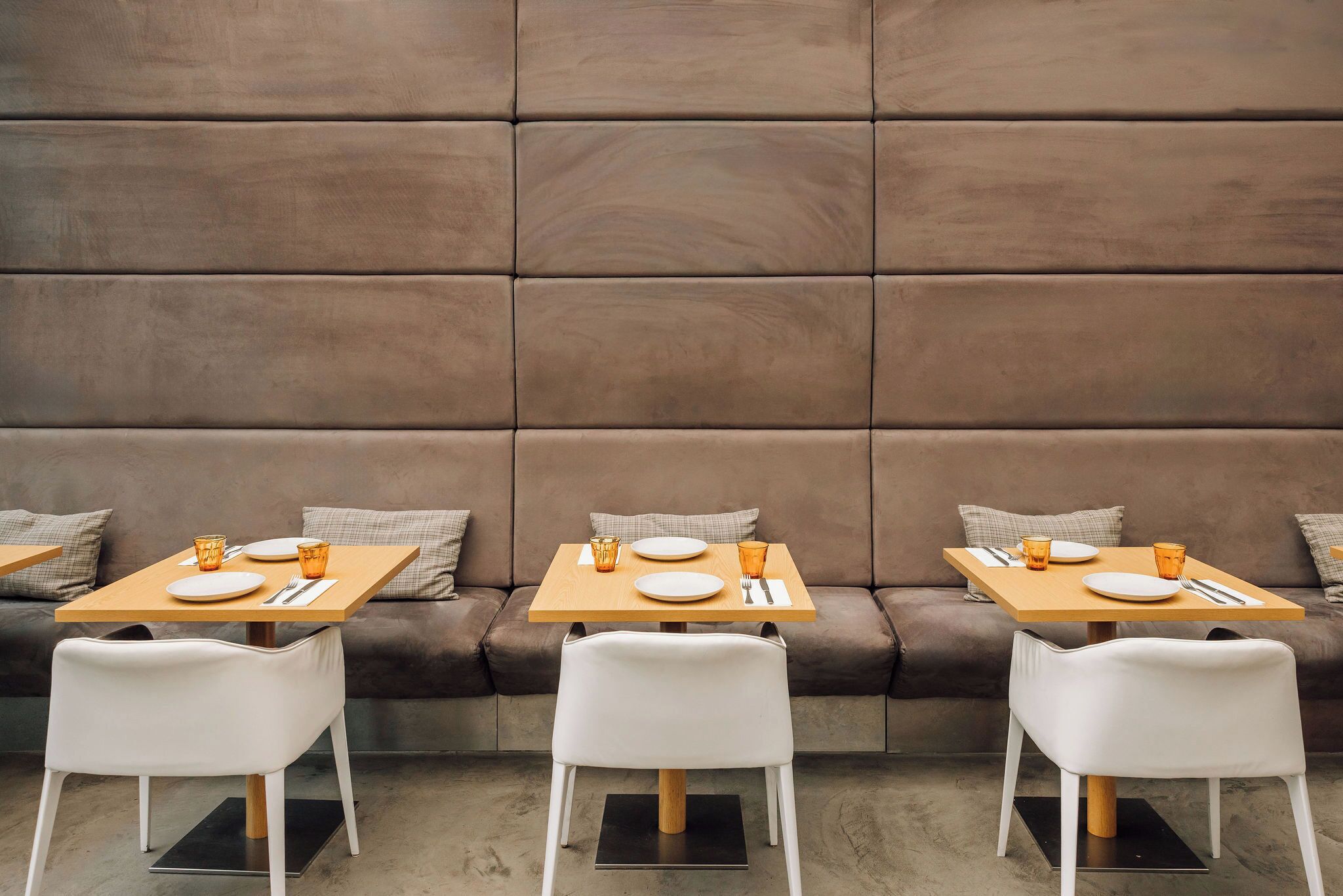 Un área de comedor con tres mesas, cada una dispuesta con platos, vasos y cubiertos. Las mesas están ubicadas frente a un amplio panel acolchado.