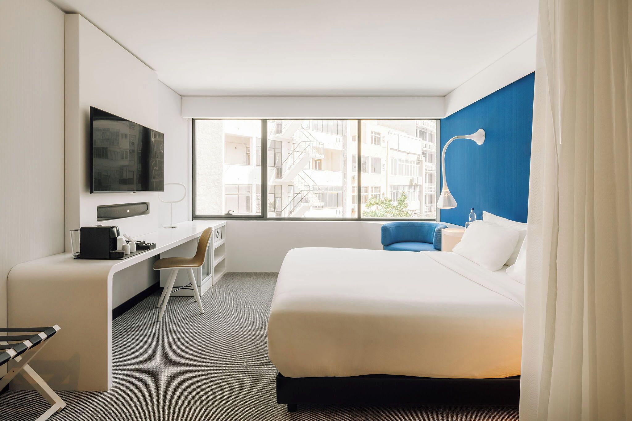A hotel room with a bed, desk, chair, TV, and a window with a city view.