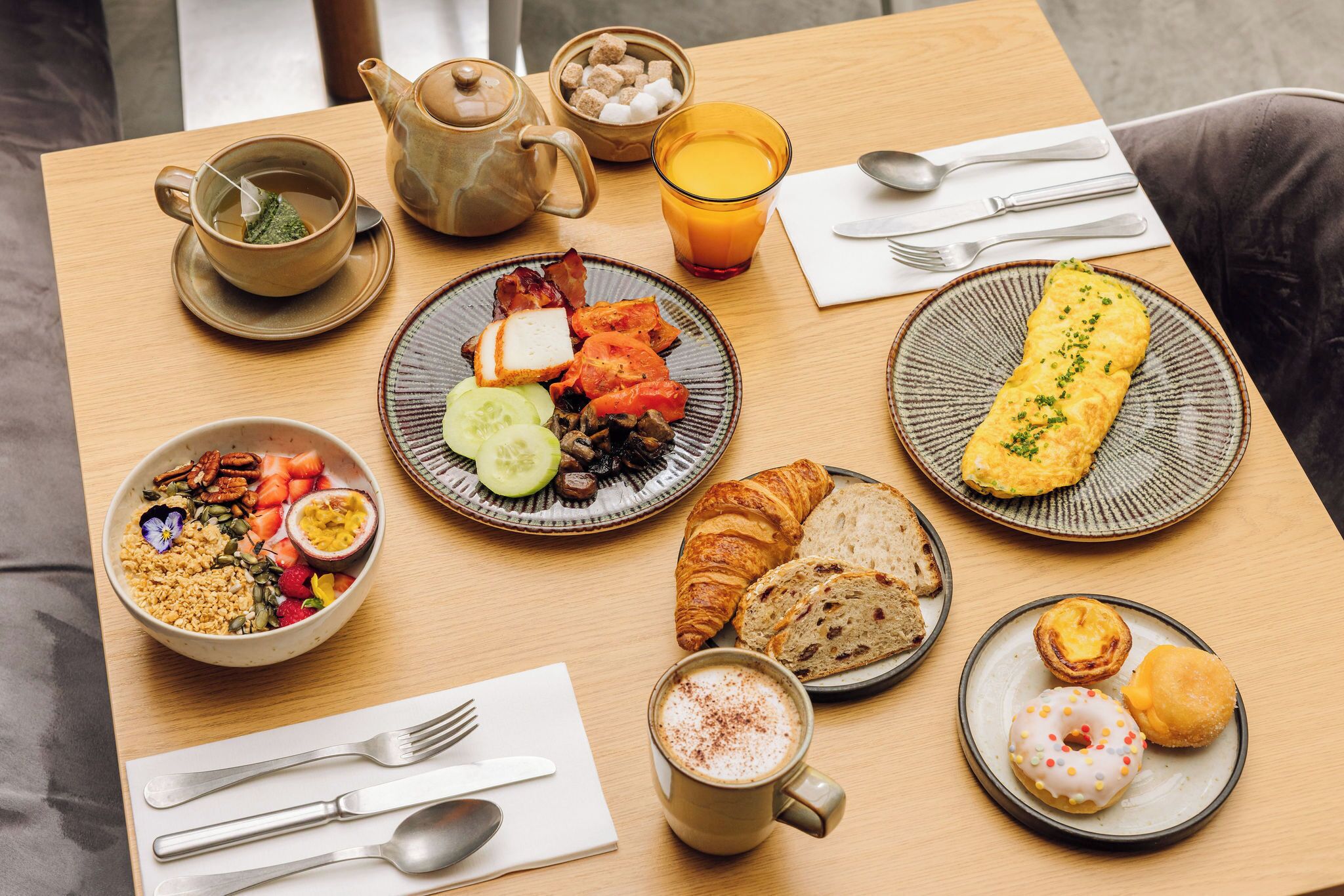 A breakfast table with various dishes, a teapot, a glass of orange juice, and a cup of coffee.