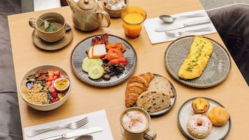 A breakfast table with various dishes, a teapot, a glass of orange juice, and a cup of coffee.
