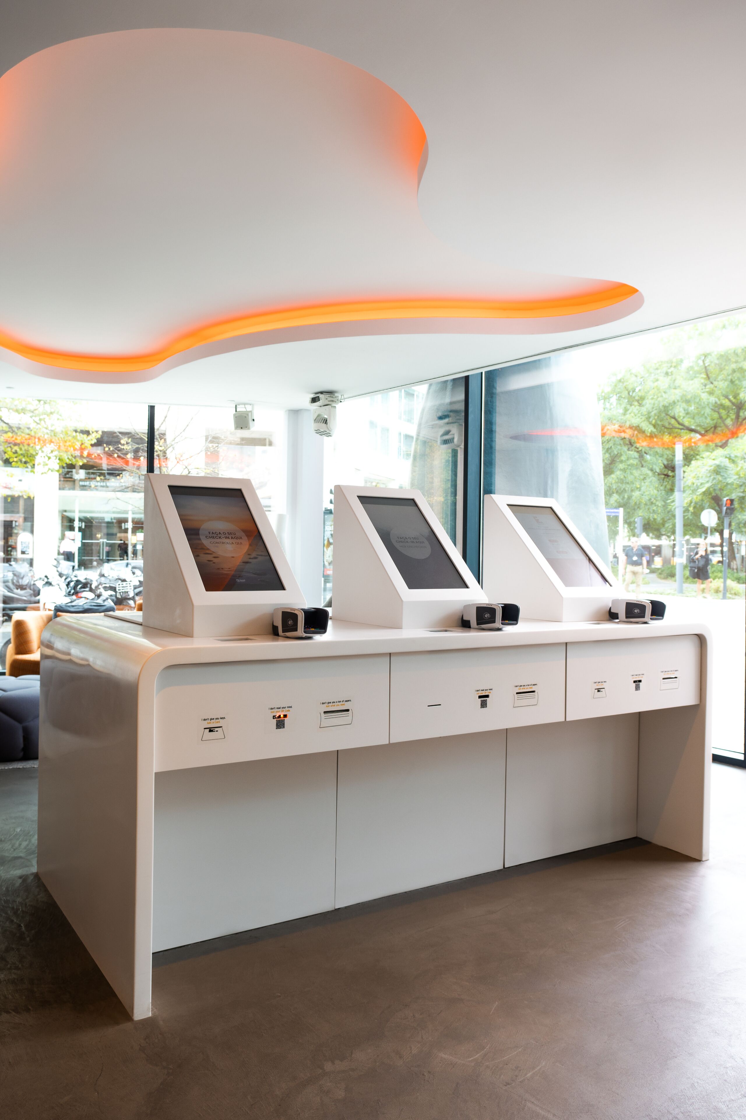 A modern reception desk with self-service kiosks, a glass window, and a view of the street.