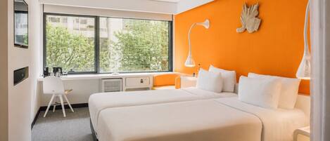 Habitación de hotel con un ventanal grande, un escritorio, dos camas y una pared de acento naranja.