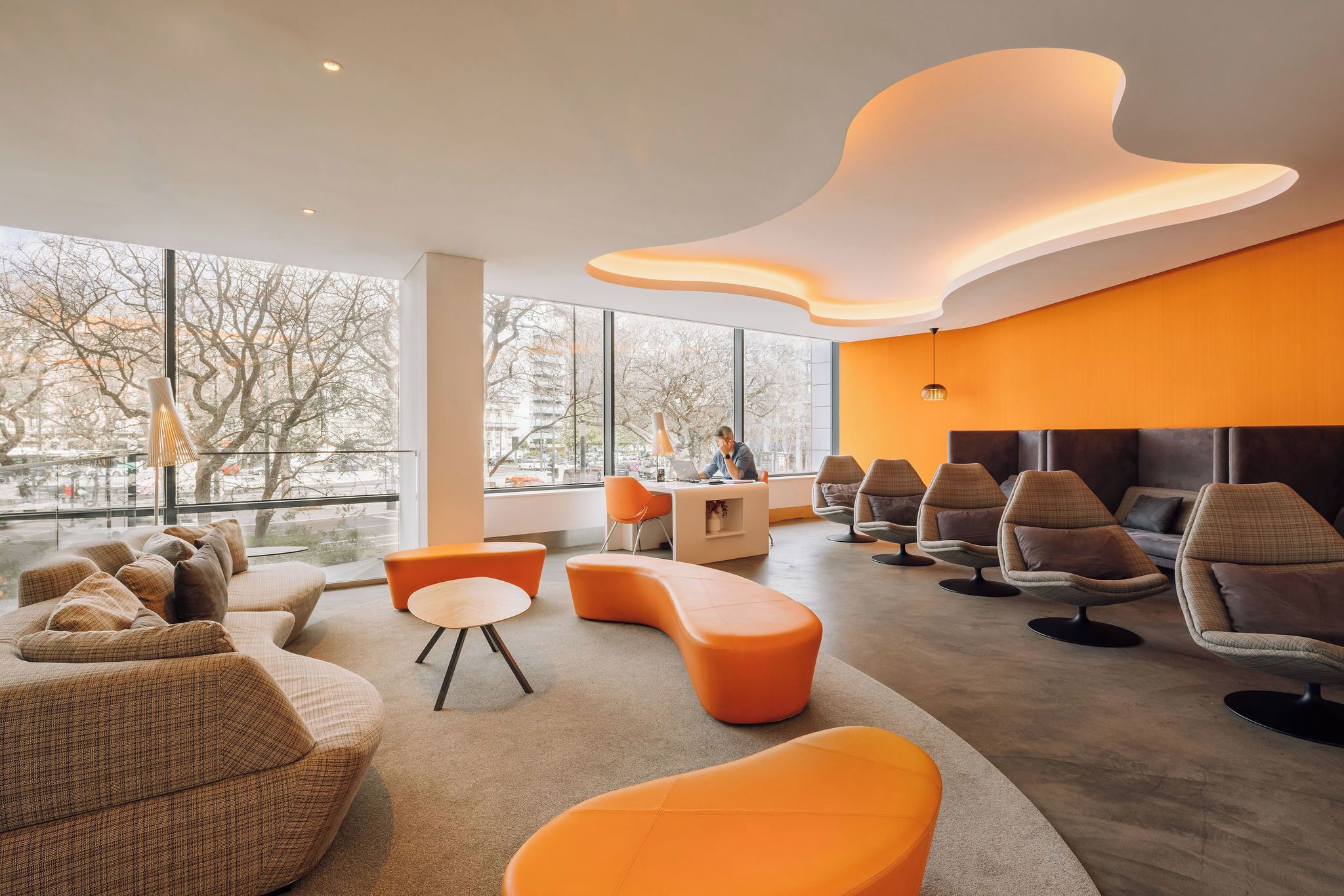 A modern interior with a curved ceiling, large windows, and a seating area with orange and brown furniture.