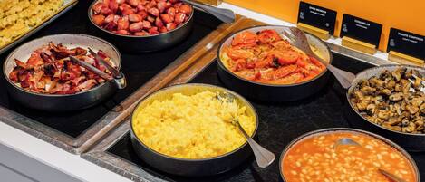 Un buffet proposant divers plats, notamment des œufs brouillés, du bacon, des saucisses, des tomates rôties, des champignons et des haricots.